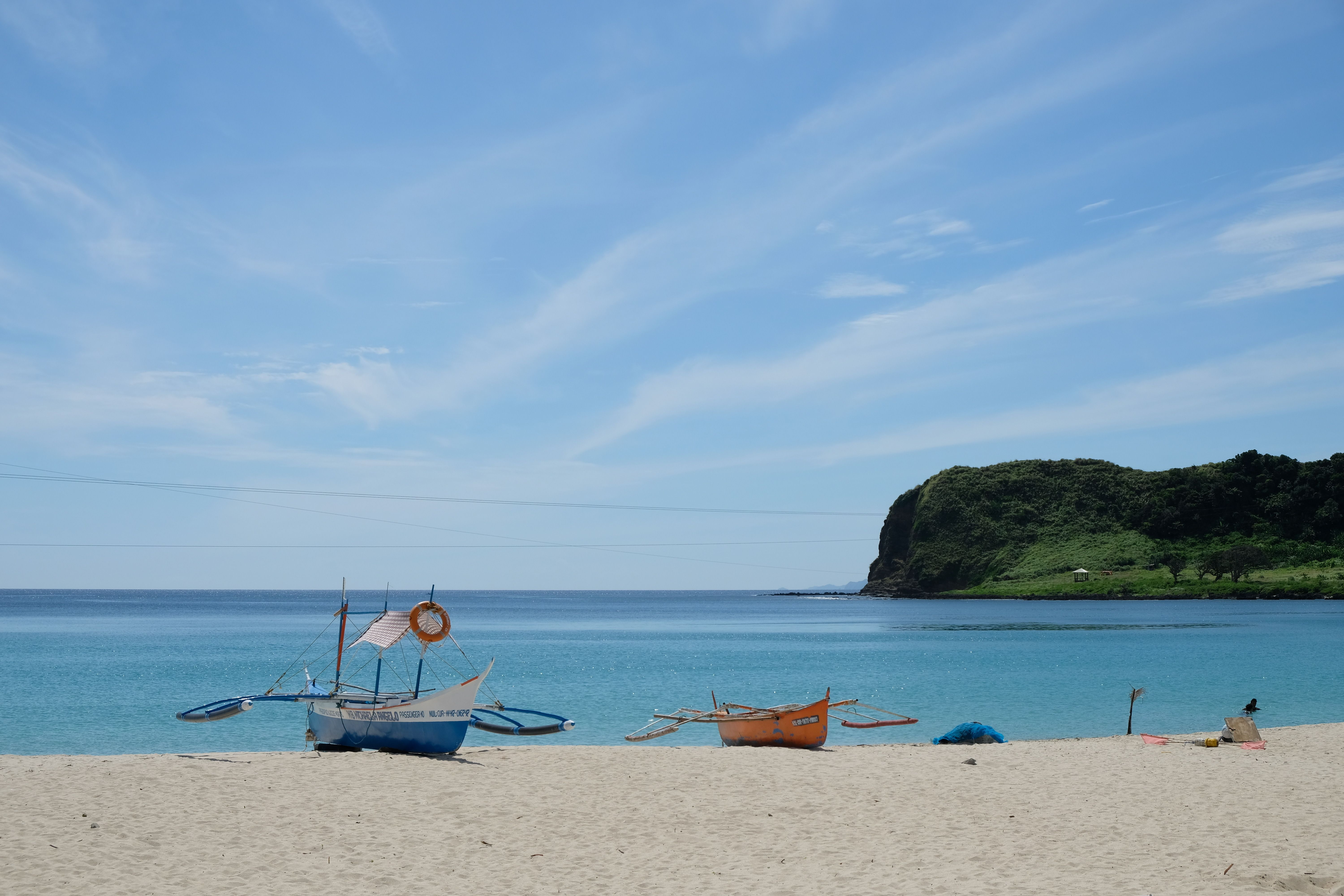 Scenic view of a beach with traditional boats in Ilocos, Philippines, under a bright blue sky.