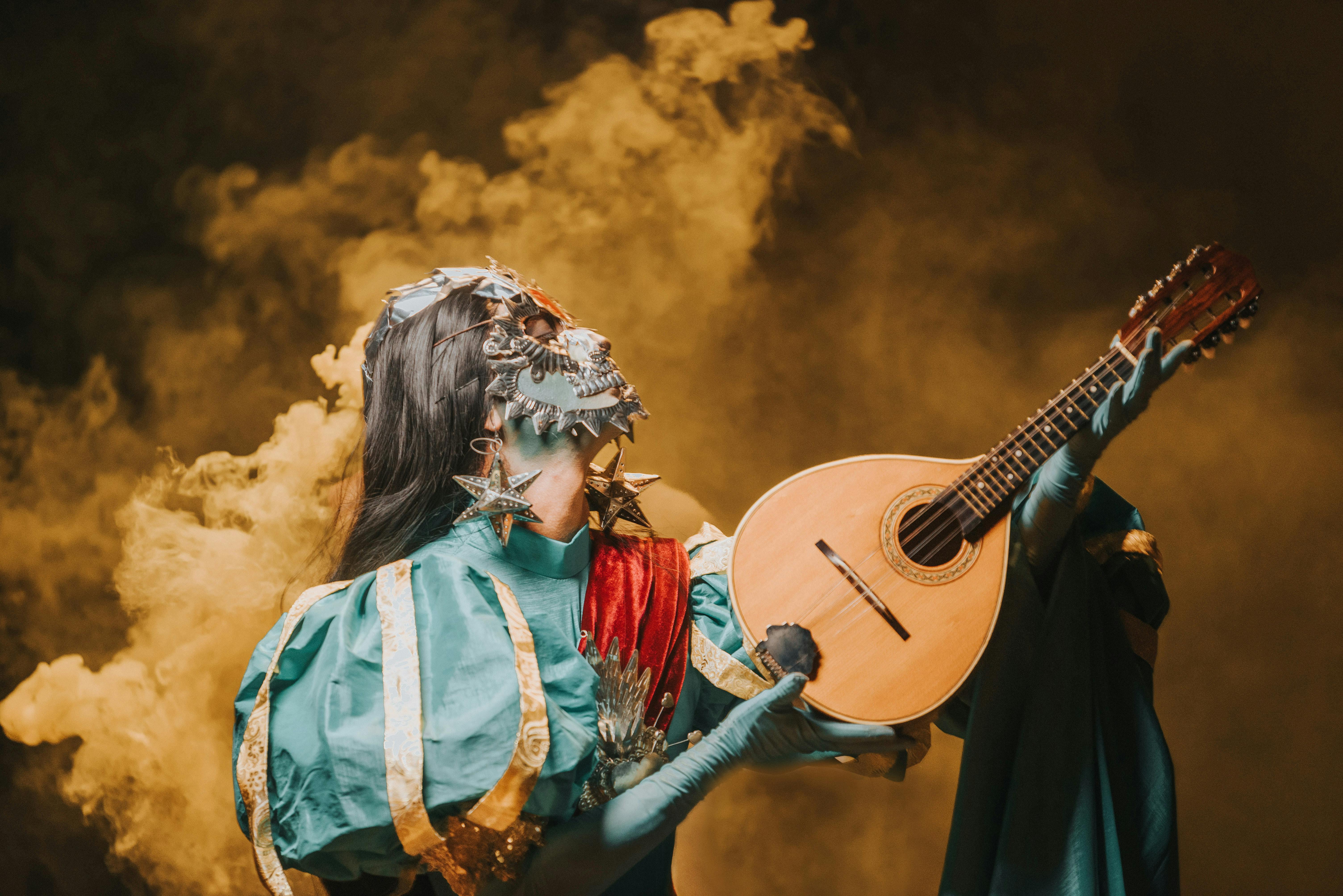 Free Masked performer in colorful costume playing mandolin amid dramatic smoke. Stock Photo