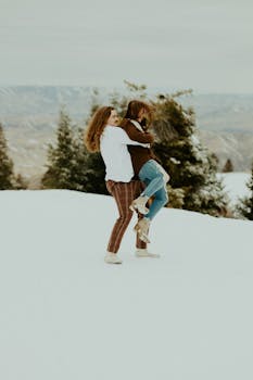 A happy couple joyfully playing in the snowy landscape amidst pine trees and scenic backdrop.