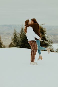 Romantic couple kissing in a snowy outdoor setting during winter with evergreen trees in the background.