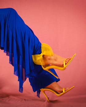Vibrant fashion photo of a woman wearing blue pants and yellow high heels on a pink background.
