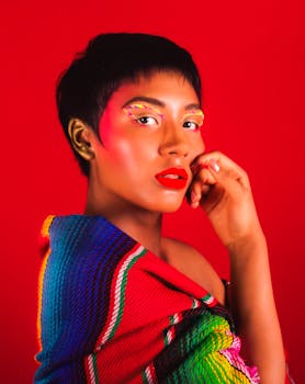 A striking portrait of a woman with creative makeup, vibrant red background, and colorful attire.
