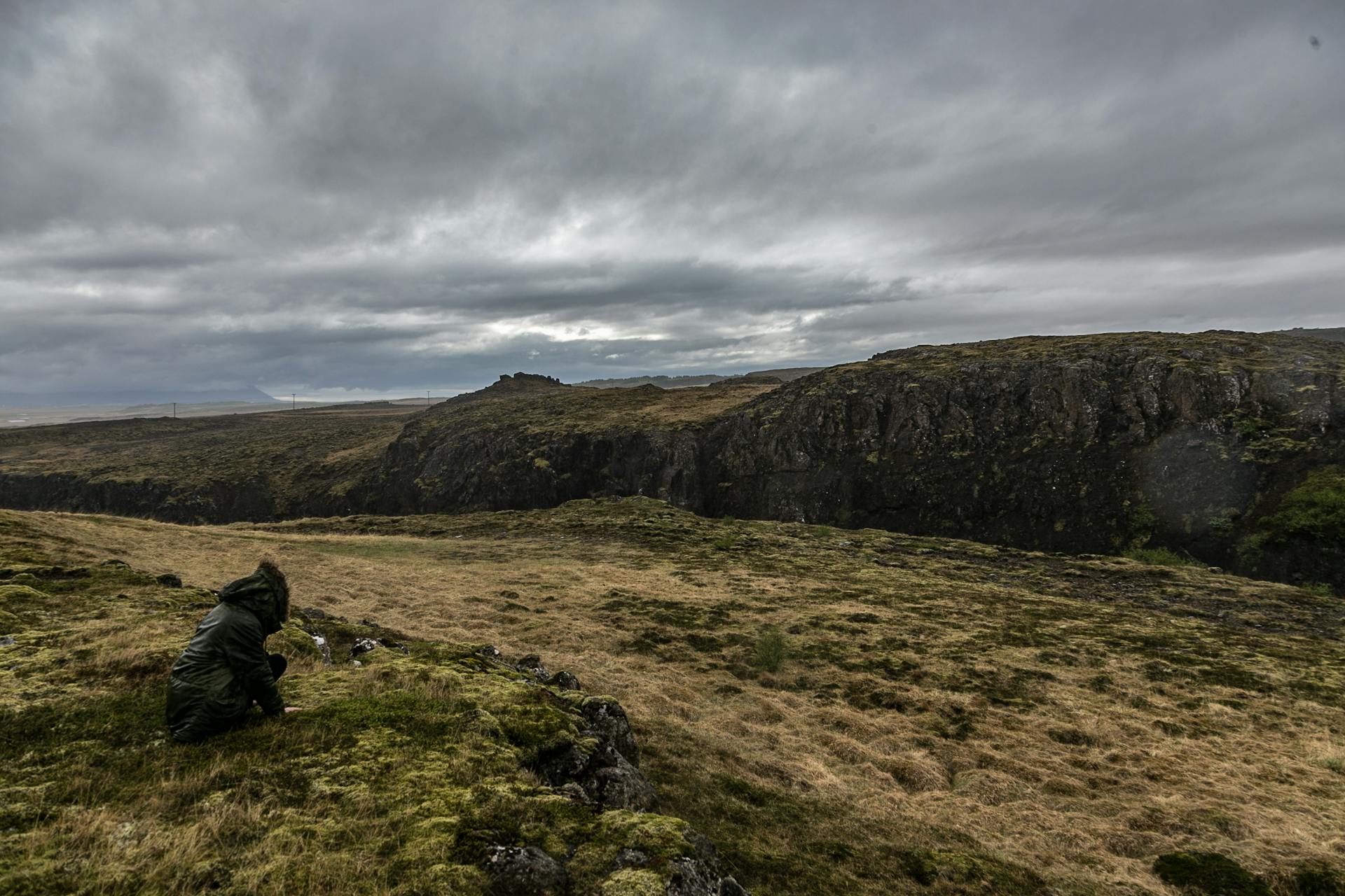 A lone traveler in a raincoat admires the rugged Icelandic terrain under a moody overcast sky.