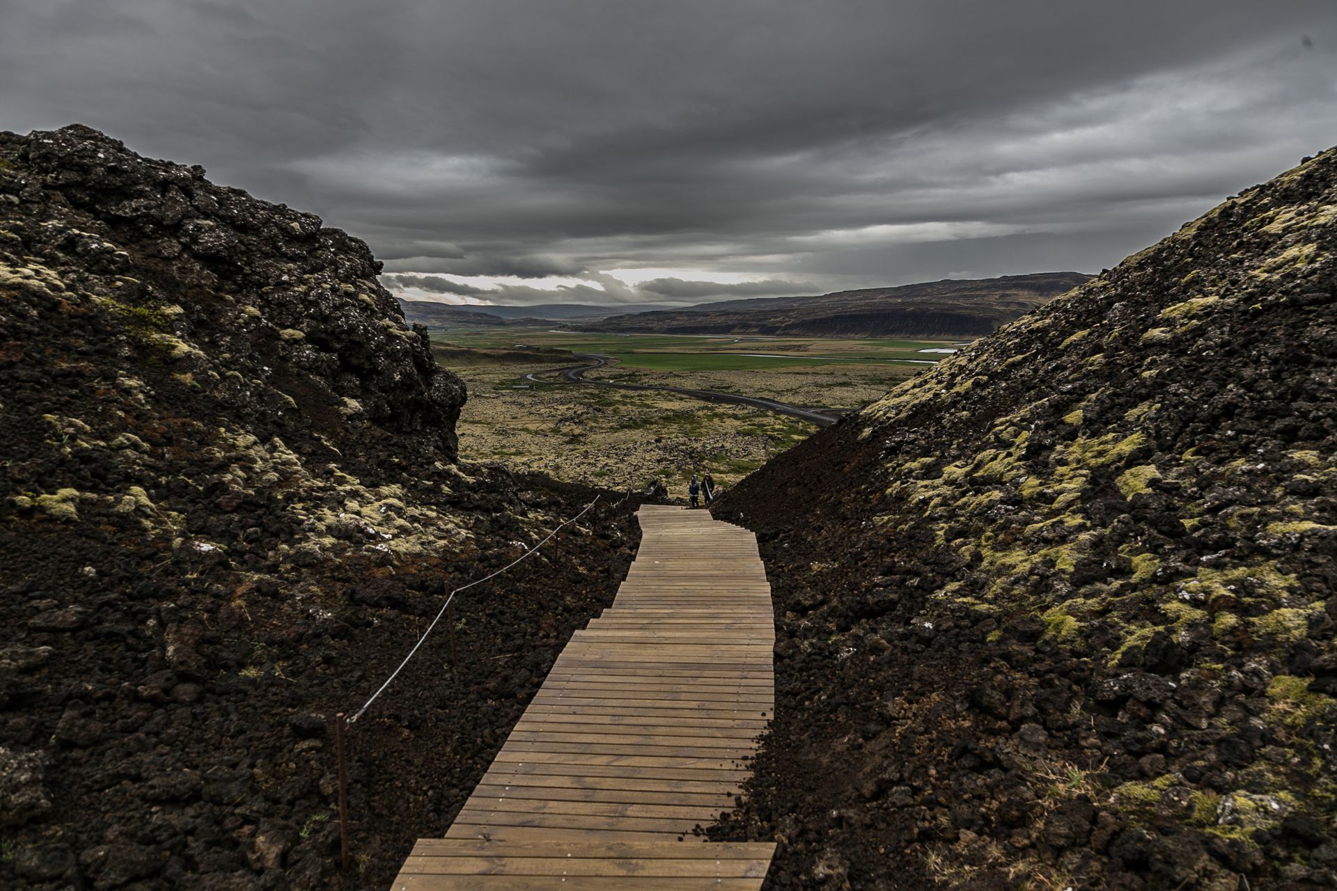Explore the dramatic volcanic landscape of Iceland along a scenic wooden pathway framed by mossy rocks.