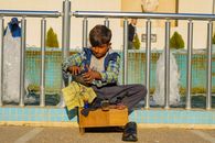 A young boy shines shoes by a fountain in Sulaymaniyah, showcasing his dedication.
