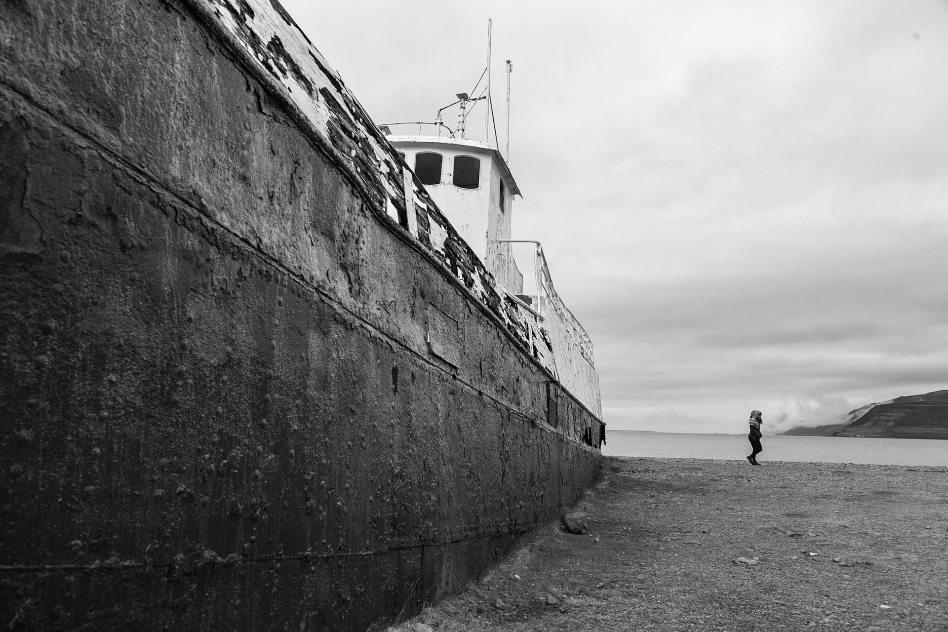 Black and white photo of an abandoned shipwreck on a desolate beach, highlighting solitude.