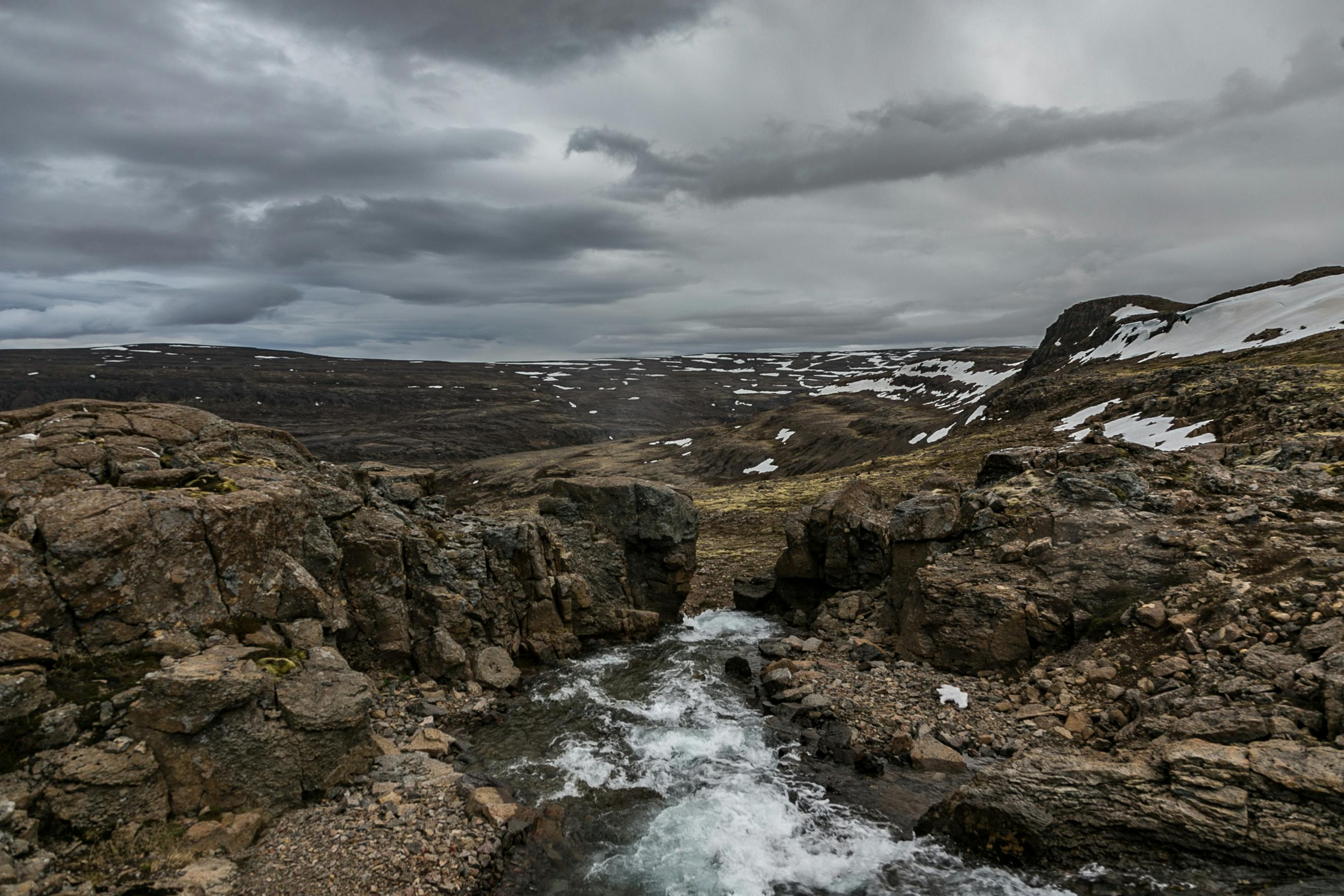 在多云的天空下，戏剧性的落基山景观中，河流流动，积雪覆盖
