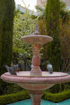 Serene garden scene in Paris featuring a classic stone fountain surrounded by lush greenery and pigeons.