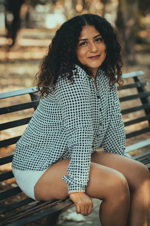 Woman in a Checkered Shirt and White Shorts Sitting on a Bench 