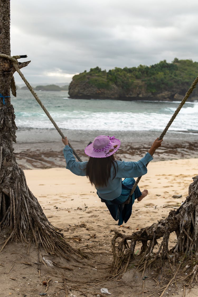 A Back View Of A Woman Swinging On The Beach