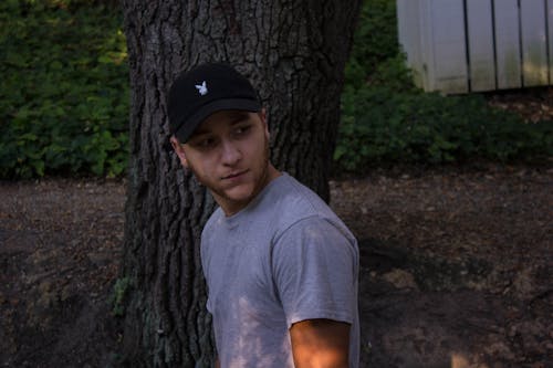 Фотография человека в серой рубашке, стоящего возле дерева