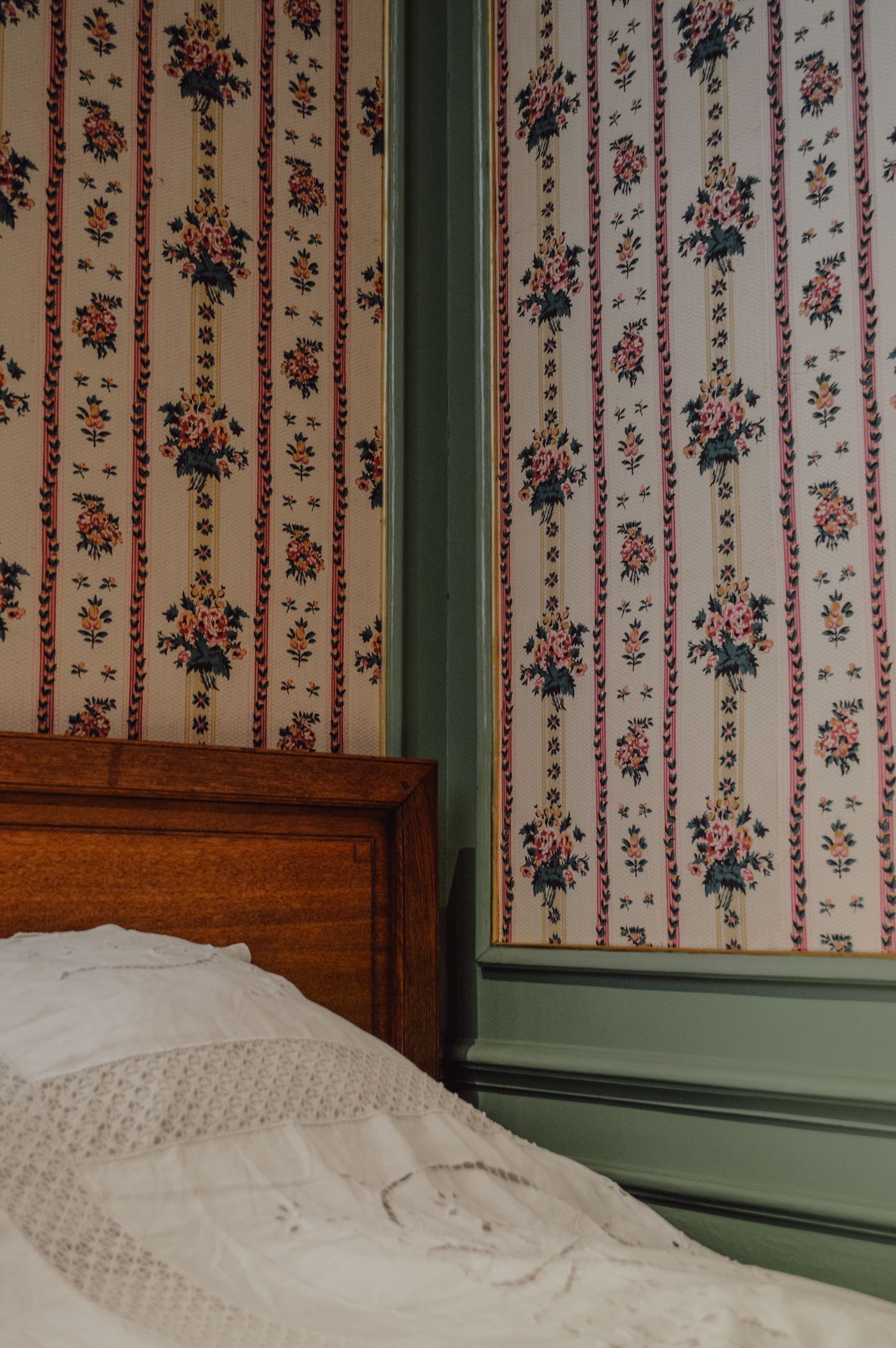 Corner of a guest bedroom with striped floral wallpaper, green panelling and an antique oak bed — photo by Neda Kekil on Pexels