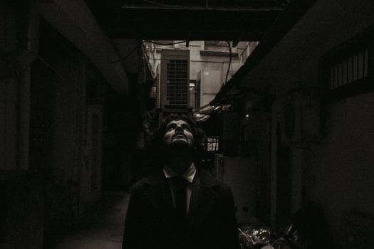 Dark and atmospheric grayscale portrait of a man looking up in a narrow Baku alley at night.