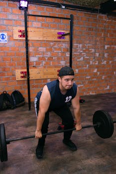 Muscular man performing deadlift exercise in a gym with a rustic brick wall backdrop.