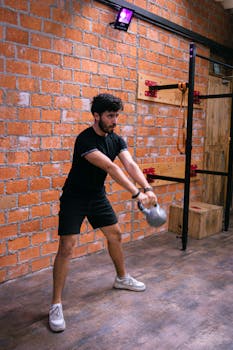Man working out with a kettlebell in a brick-walled gym for strength training.
