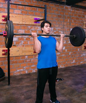 Adult male lifting a barbell in an indoor gym setting, showcasing fitness and strength.