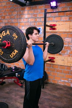 A young man in activewear lifting a barbell at a gym, focusing on strength and fitness.