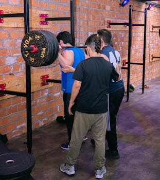Men lifting heavy barbell in Ciudad de México gym with brick wall background.