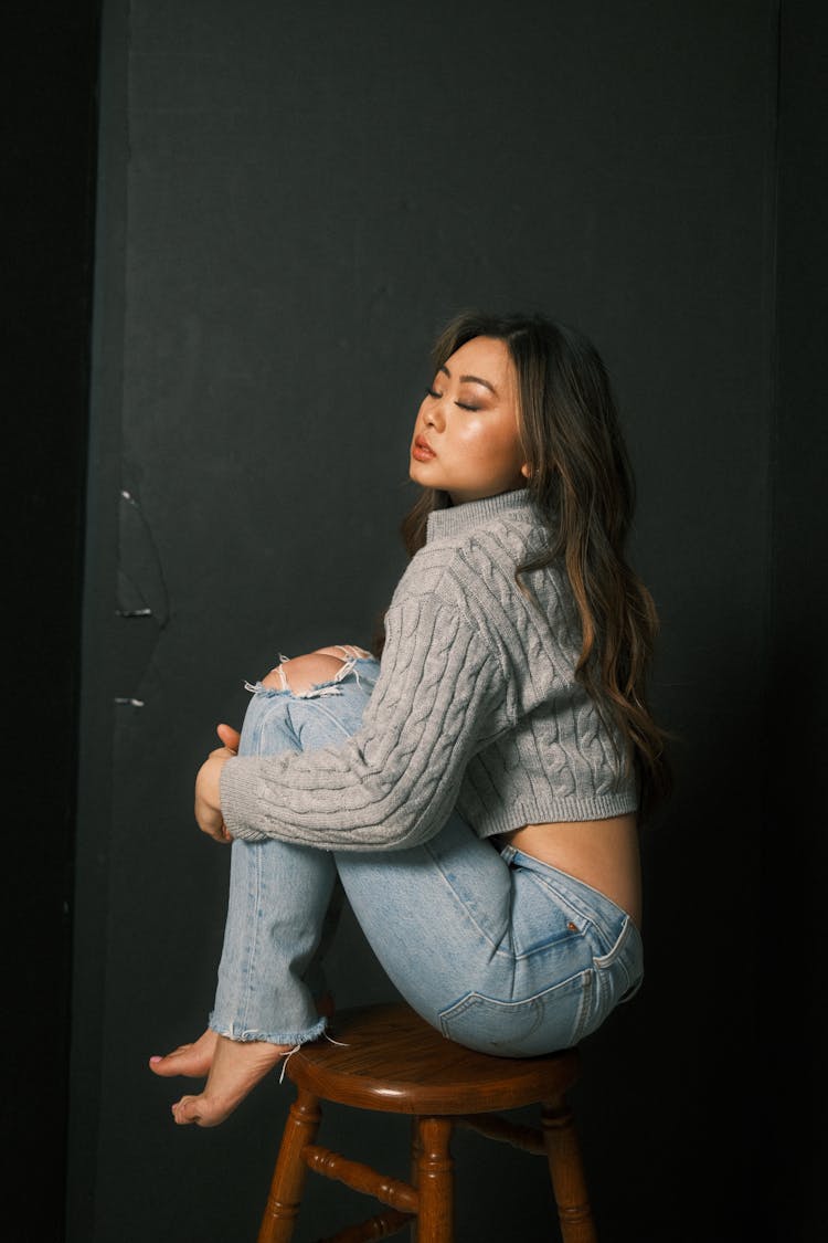 Woman Sitting On A Wooden Stool And Embracing Her Legs 