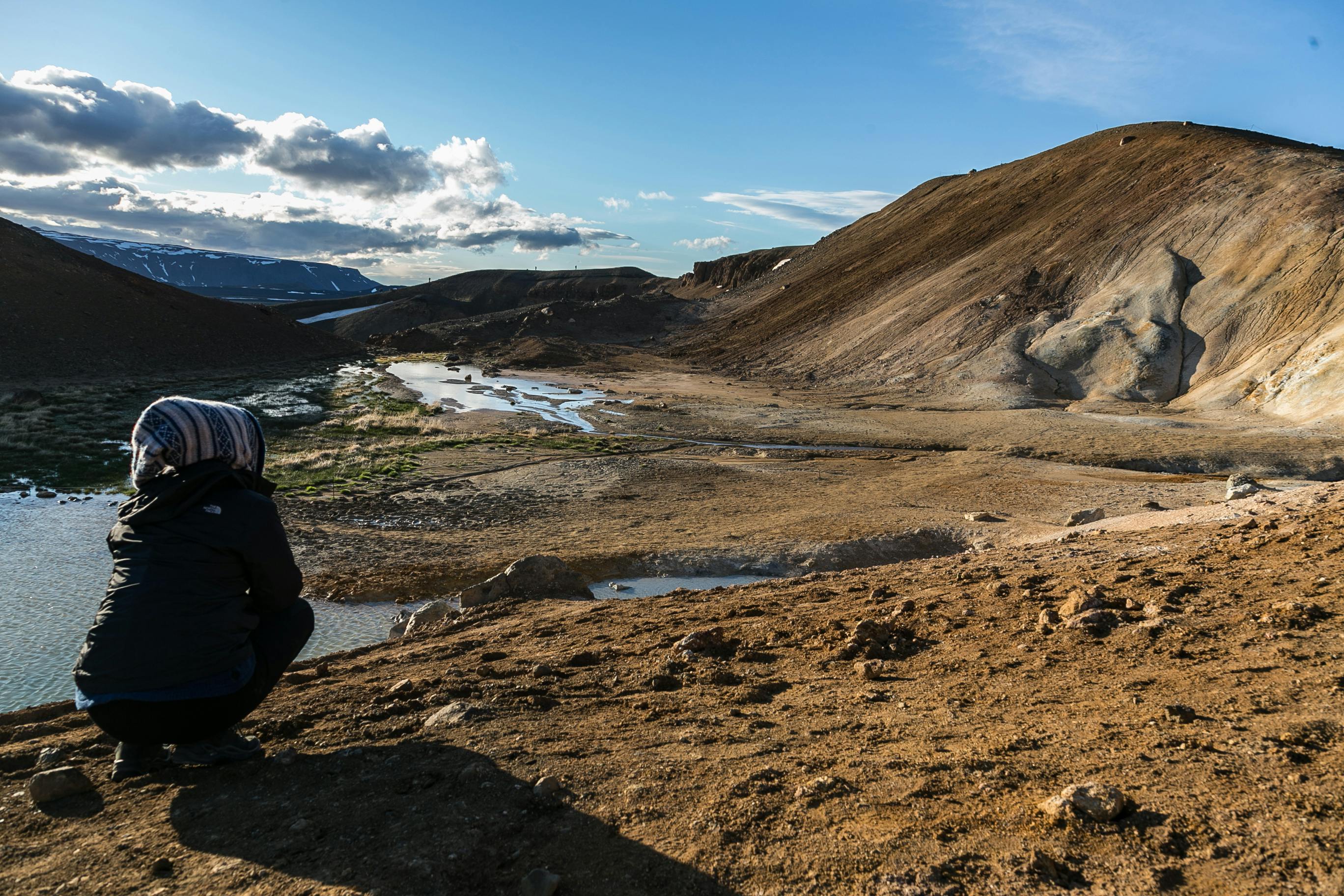 一个人蹲伏着，在明亮的天空下欣赏广阔的山景和流动的河流