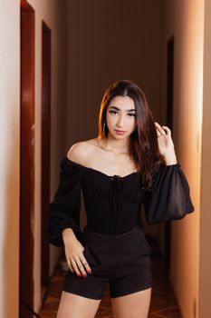 Stylish woman in an off-shoulder black outfit posing confidently in a hallway.