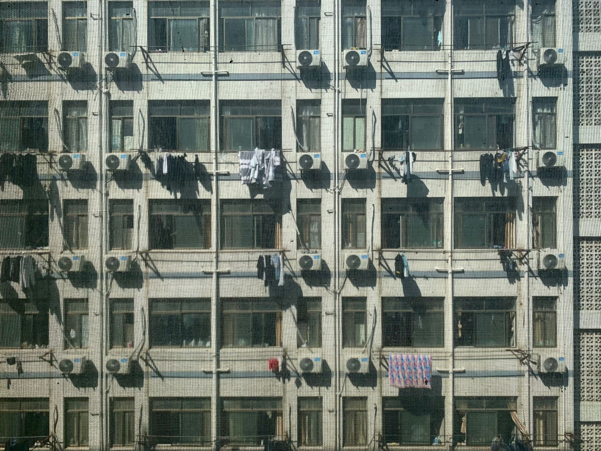 Facade of apartment building with air conditioners and drying clothes in an urban setting.