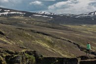 一名身穿绿色夹克的妇女站在悬崖上，俯瞰着冰岛白雪皑皑的山峰