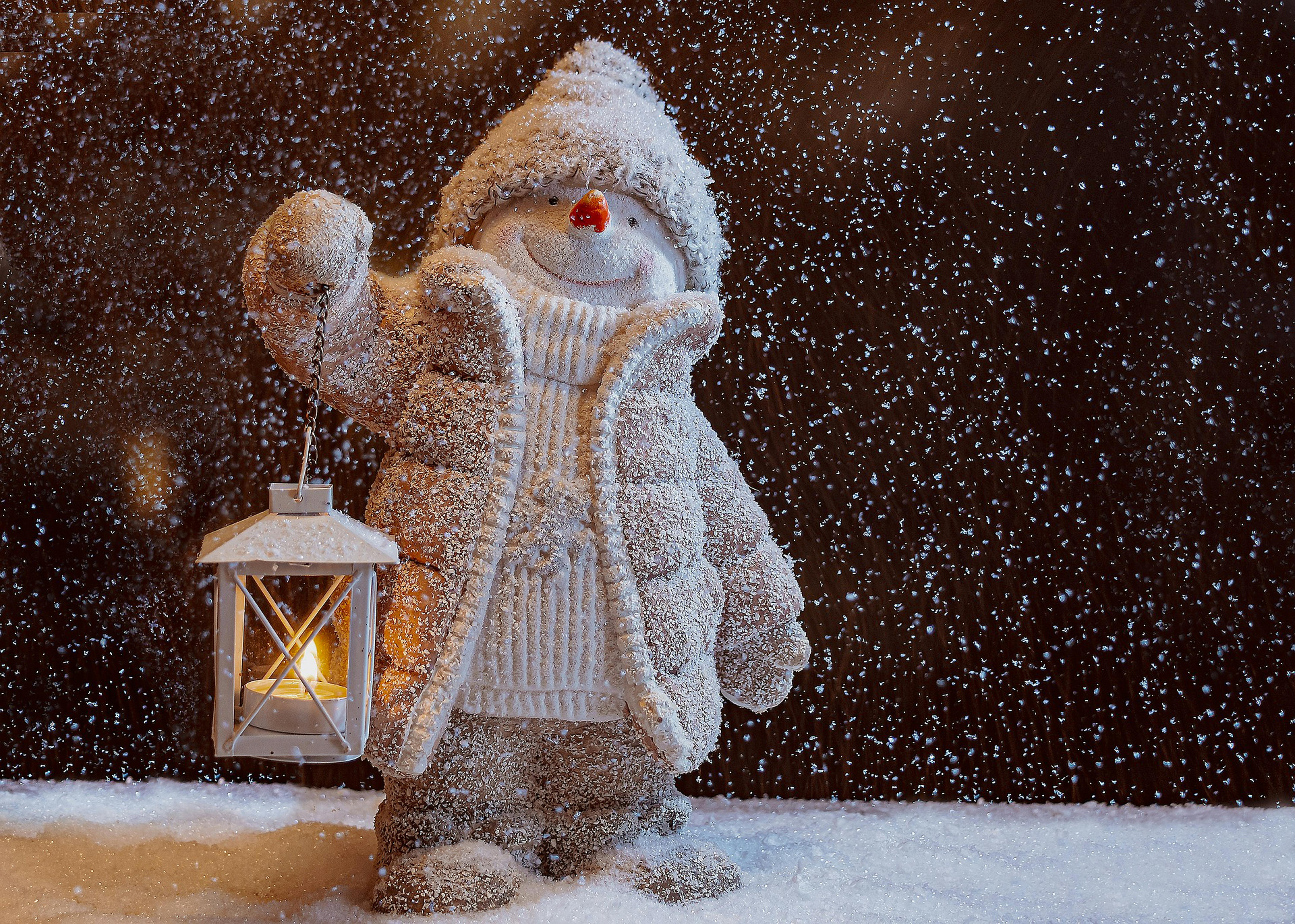 Adorable snowman figurine holding a lantern, surrounded by falling snow, creating a cozy winter atmosphere.