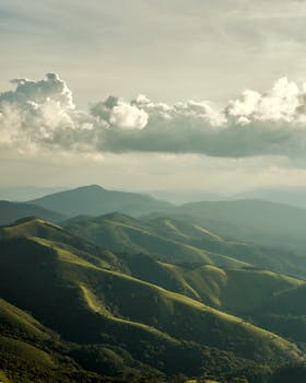 A stunning vista of lush green hills under a dramatic cloud-filled sky, captured at twilight.