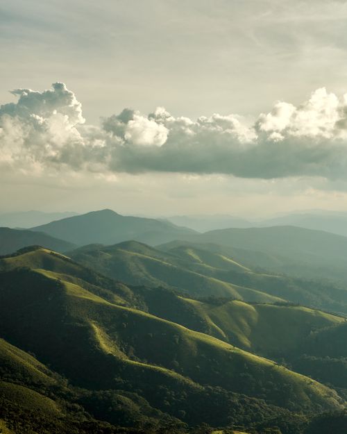 Free A stunning vista of lush green hills under a dramatic cloud-filled sky, captured at twilight. Stock Photo