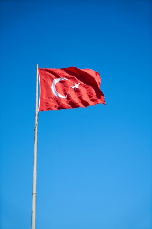 Free Vibrant Turkish flag waving on a flagpole against a cloudless blue sky symbolizing freedom and patriotism. Stock Photo