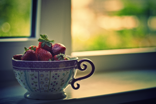 Fresh strawberries in a decorative cup by a window with soft focus background.