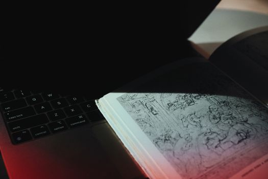 An open book placed on a backlit laptop keyboard, highlighting intricate sketches with dramatic lighting.