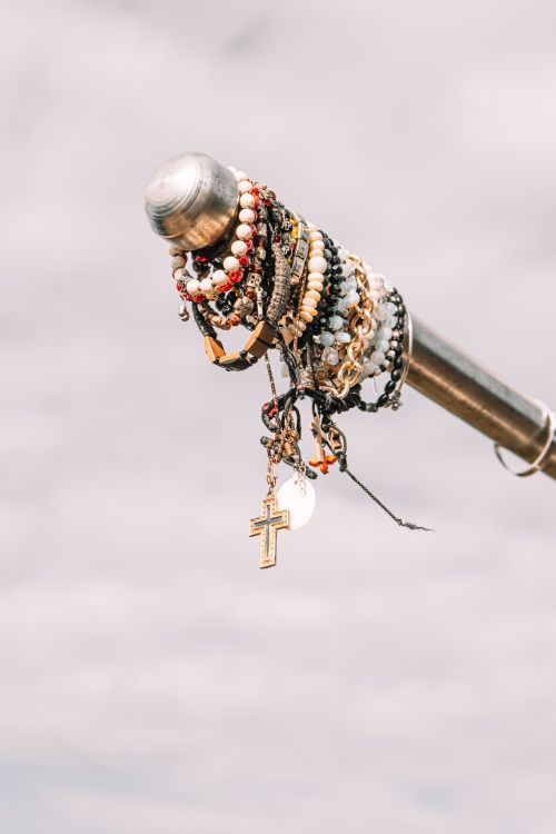 Free Artistic display of colorful beaded bracelets and cross pendant hanging on a metallic pole. Stock Photo