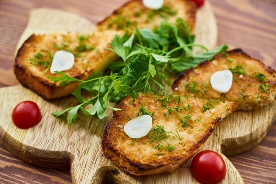 Golden garlic toasts sprinkled with dill and garlic slices, topped with greens and cherry tomatoes