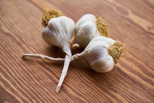 Close-Up Photo of Three Garlic on Wooden Surface