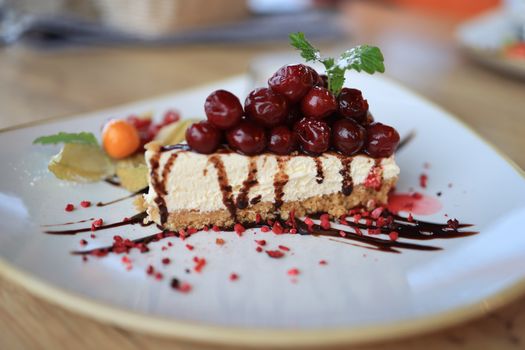 Close-up of a delectable cherry-topped cheesecake slice with chocolate drizzle on a ceramic plate.