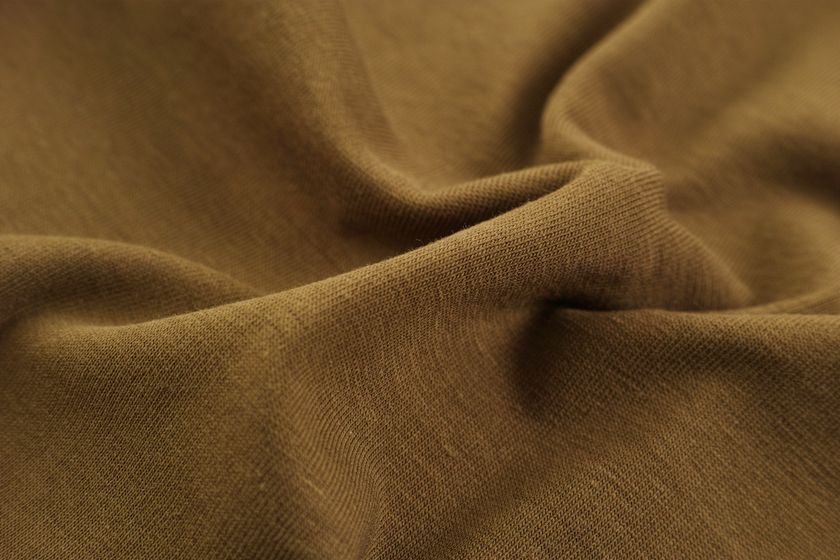 Close-up of a soft olive-brown cloth falling in fluid folds, the surface matte with fine creases across it.