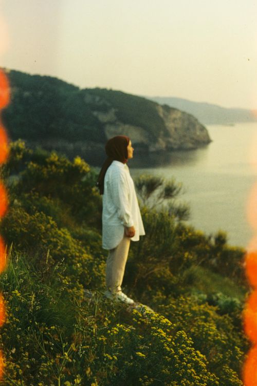 Free Serene scene of a woman standing on a cliff, overlooking the sea during sunset. Stock Photo