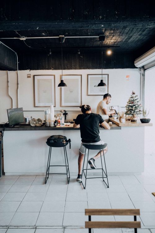 Free Modern café with customer at counter, enjoying a drink while barista prepares coffee. Bright, welcoming atmosphere. Stock Photo