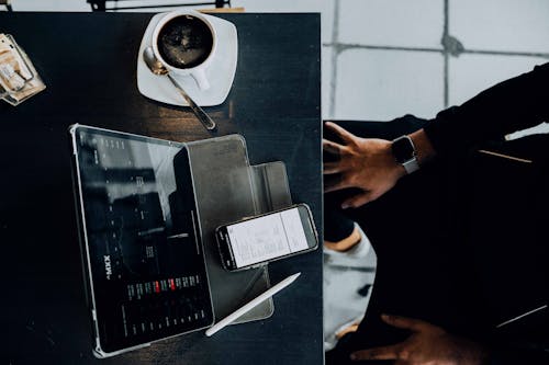 Free Person Sitting at a Table in a Cafe and Looking at a Tablet and Smartphone Screen  Stock Photo