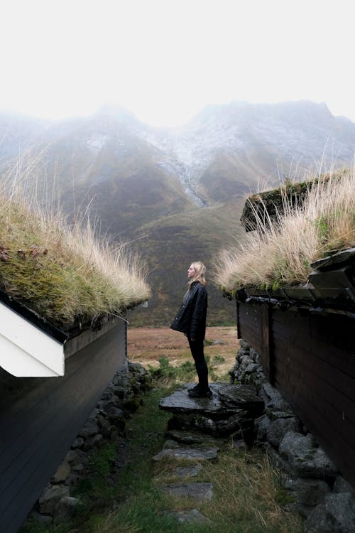 Woman Standing between Wooden Huts in Mountains 