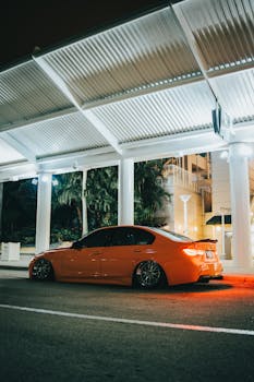 A luxurious red sports car parked under urban lights on a city street at night.