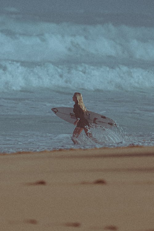 Photograph of a Woman Running while Carrying a Surfboard