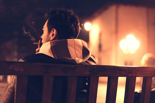 Shallow Focus Photography of Man Sitting on Bench While Smoking