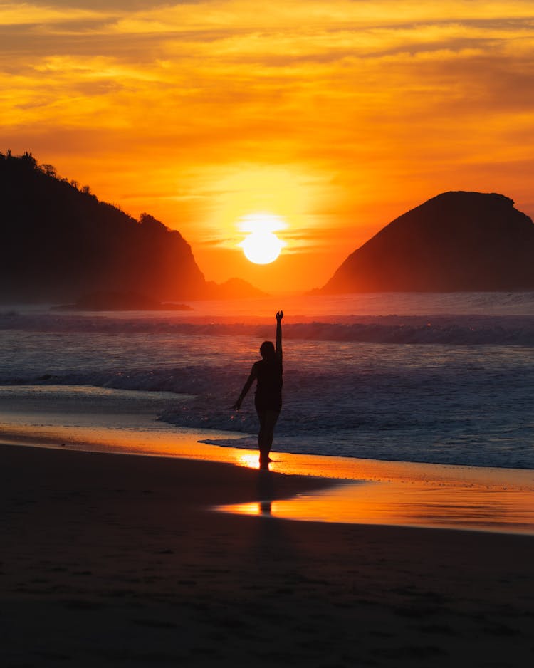 Person With Arm Raised On Beach At Sunset