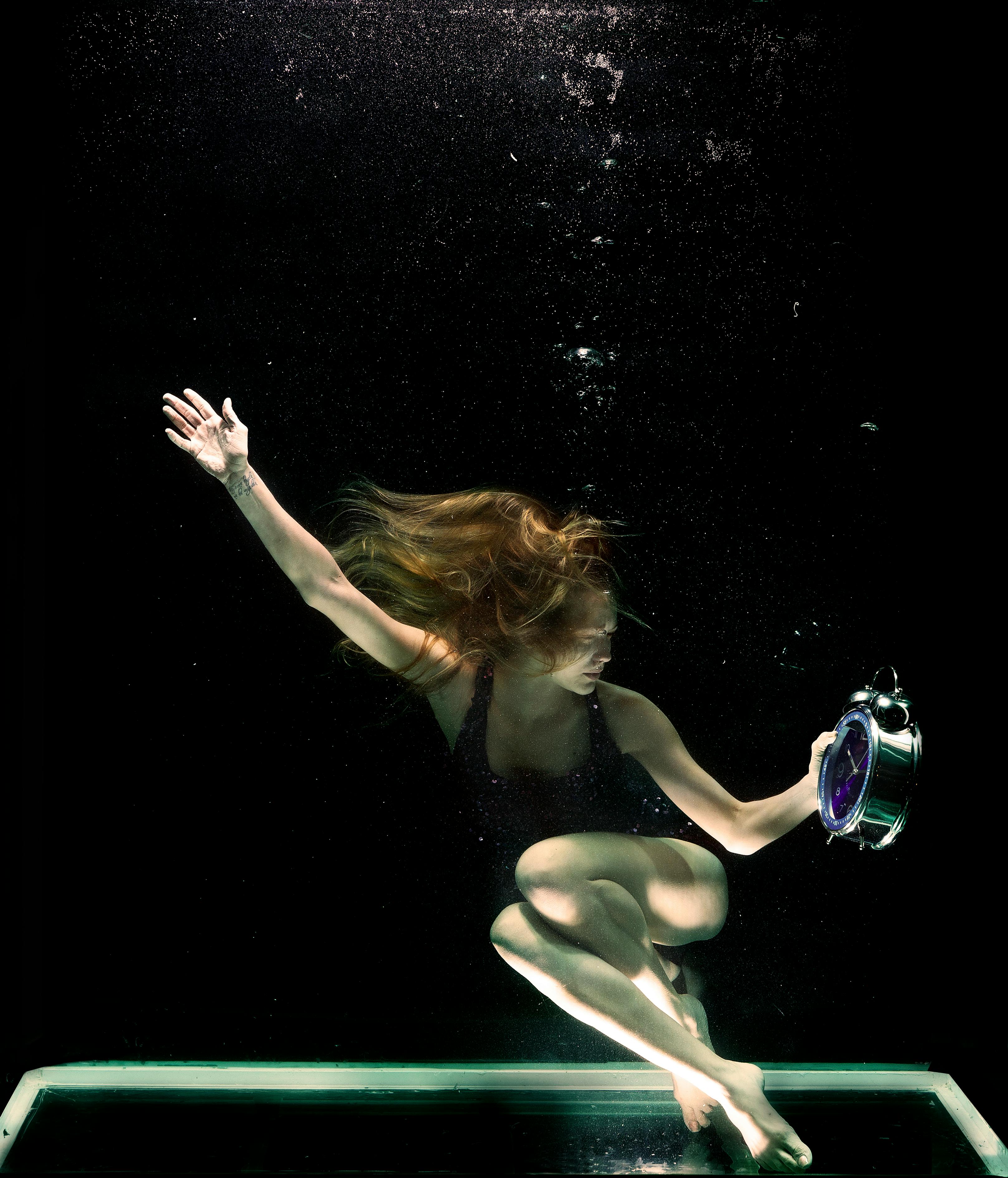 woman underwater holding round gray clock