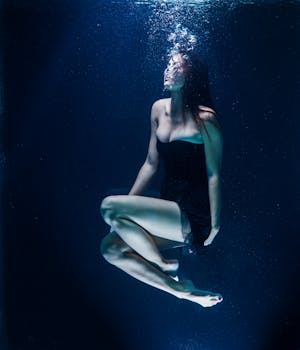 一位身着黑色连衣裙的女子在水下优雅地摆着姿势，散发出优雅的气息