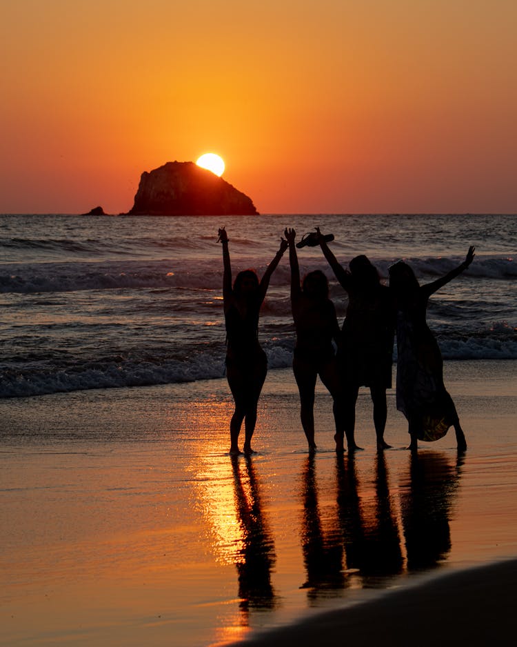 Silhouette Of Women Standing Near Body Of Water During Sunset