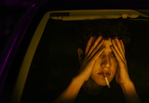 Free Young man sits with a cigarette, reflecting and pensive, inside a car at night. Stock Photo